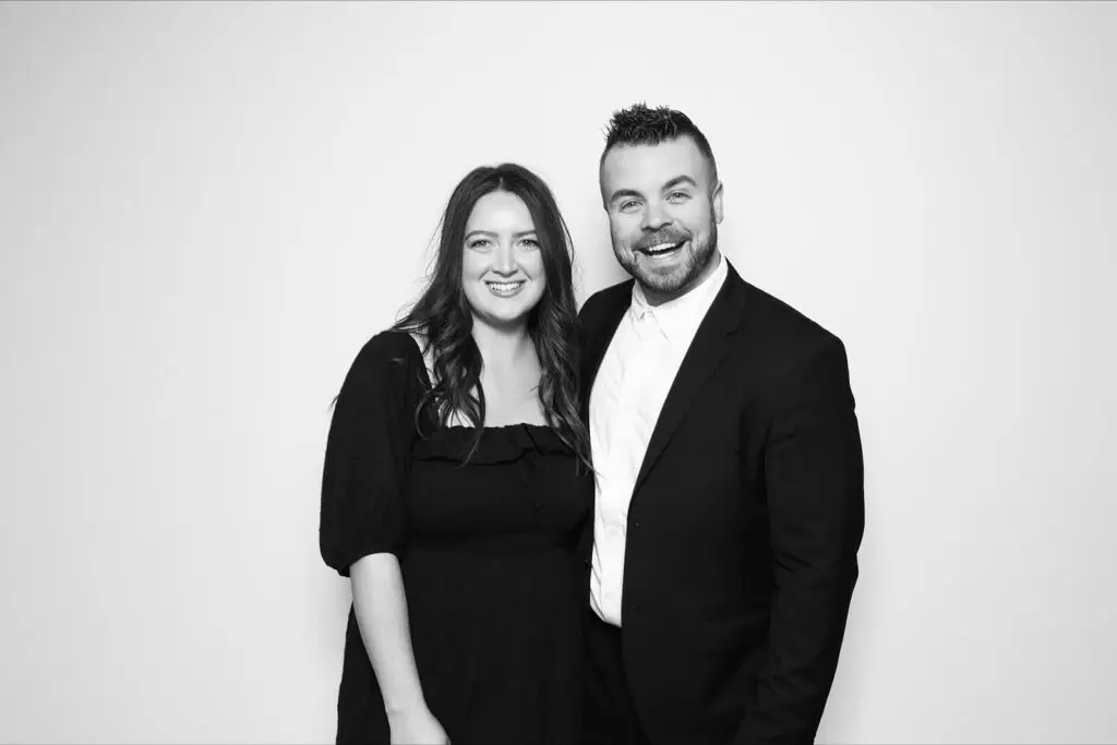 A woman in a black dress and a man in a black suit smile together for a black and white glam photo booth portrait at a corporate banquet.