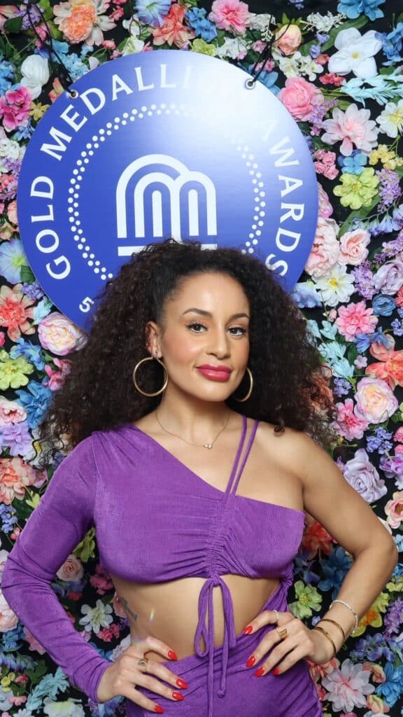 Corporate celebrations photo booth Kansas City guest posing at a branded Gold Medallion Awards photo activation with a floral backdrop.