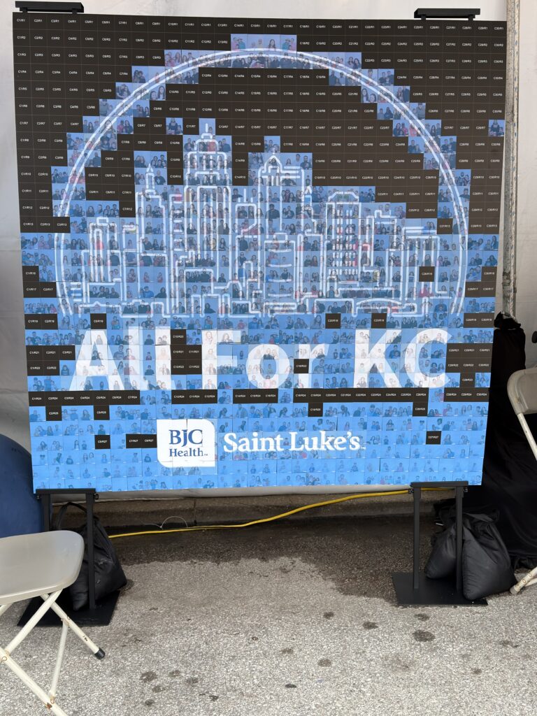saint lukes photo mosaic wall completed plaza art fair Nearly finished photo mosaic wall made from guest portraits, forming the All For KC Kansas City skyline with the BJC Health and Saint Luke's logos, on display in the Saint Luke's tent at the 2026 Plaza Art Fair.